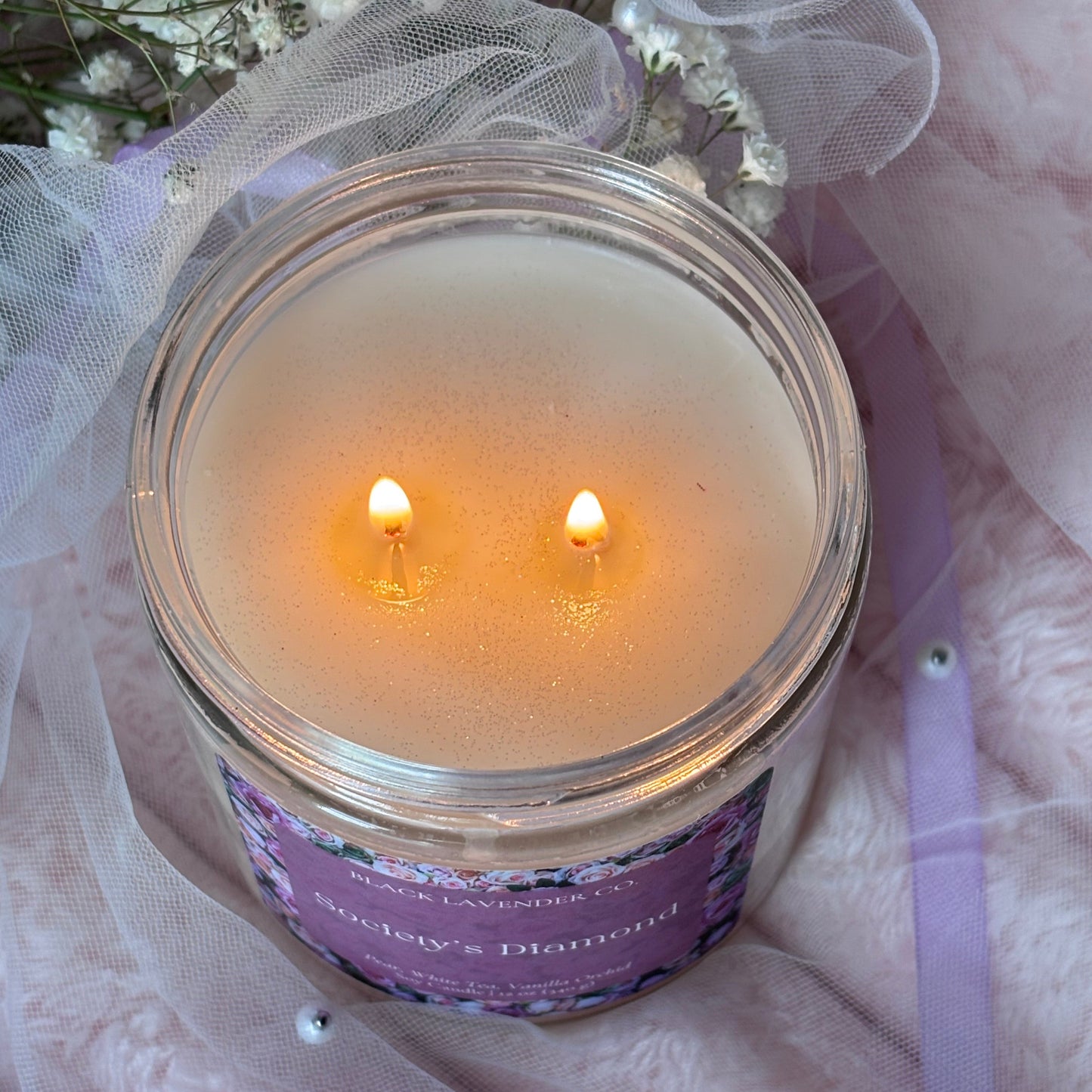 Candle in a glass jar with a purple label on a soft pink fabric background