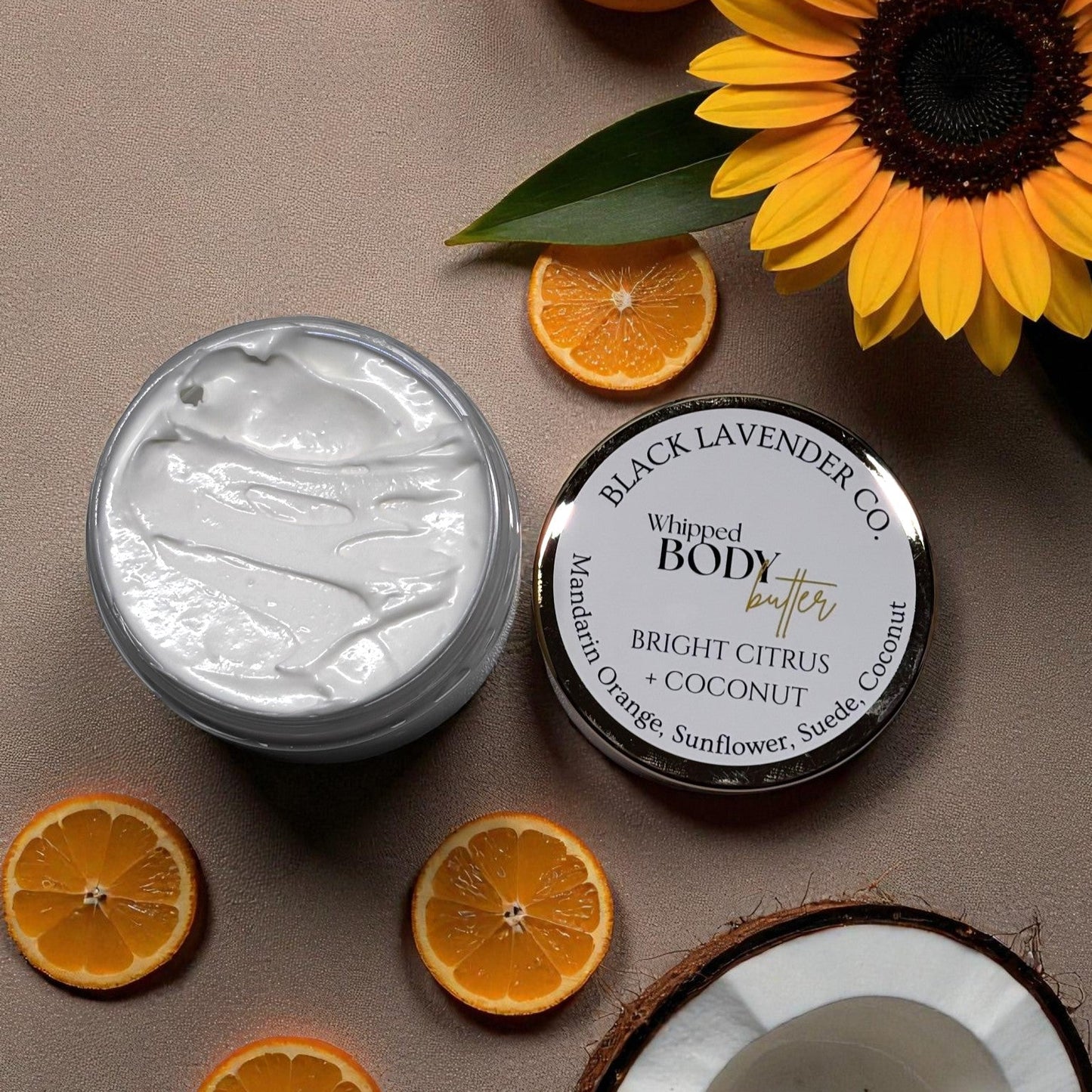 Whipped body butter jar with a sunflower and oranges on a brown background