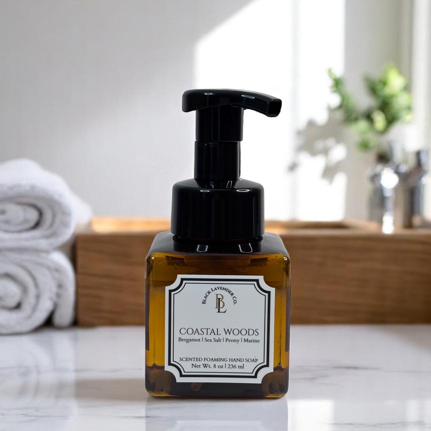 A pump bottle of Coastal Woods foaming hand soap with a label, on a bathroom countertop.
