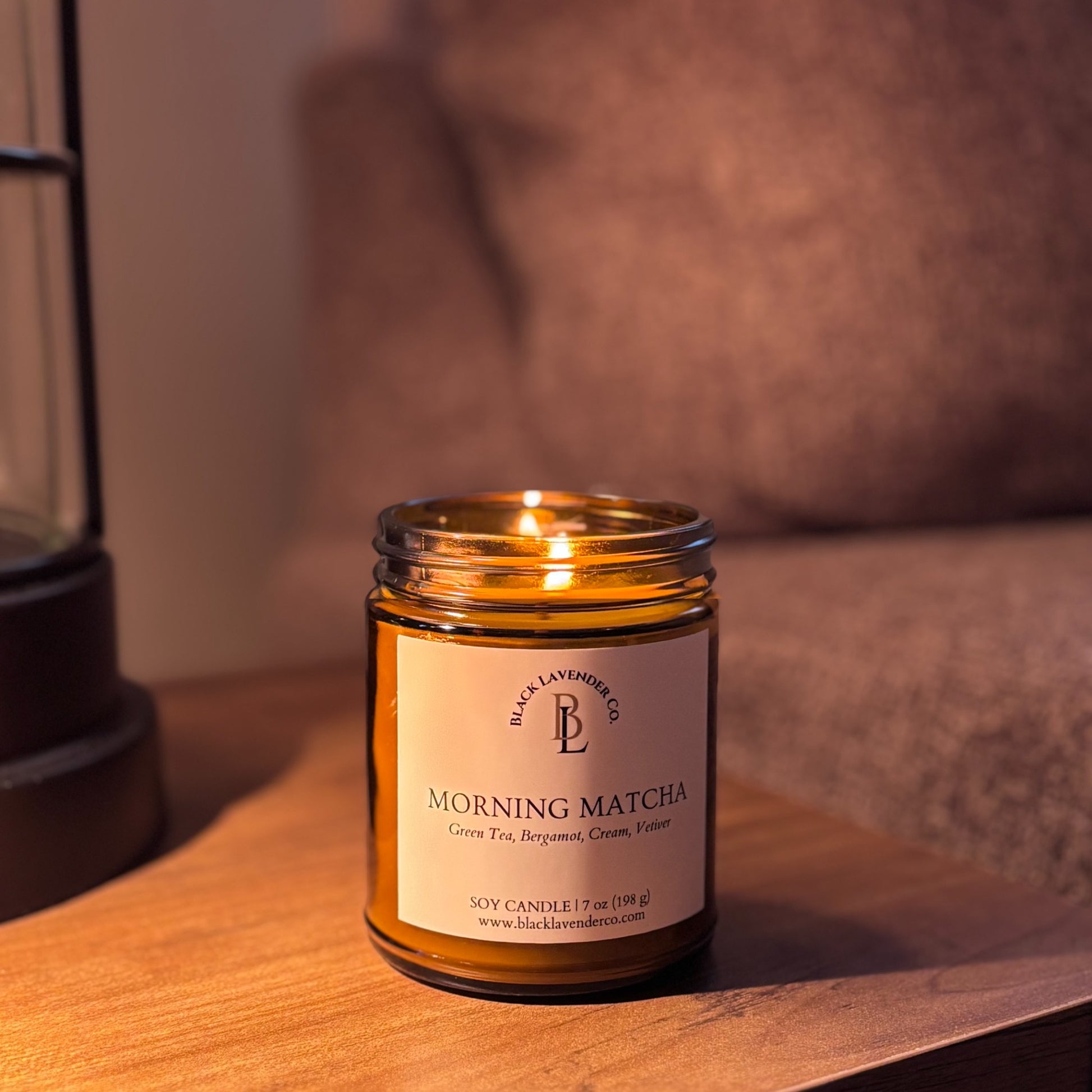 Candle in a jar labeled 'Morning Matcha' on a wooden surface with a lifestyle background