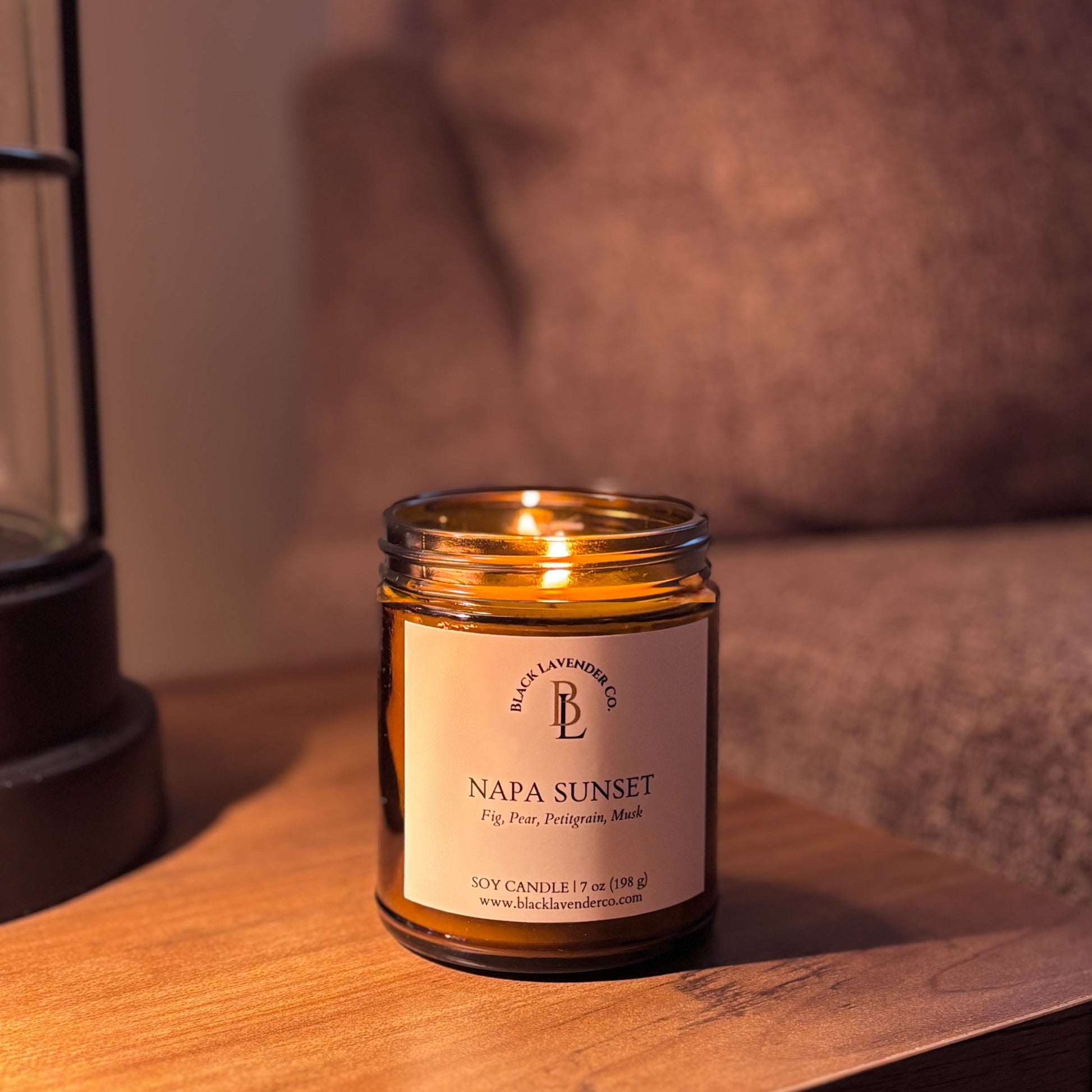 Candle labeled 'Napa Sunset' on a wooden surface with a lifestyle  background