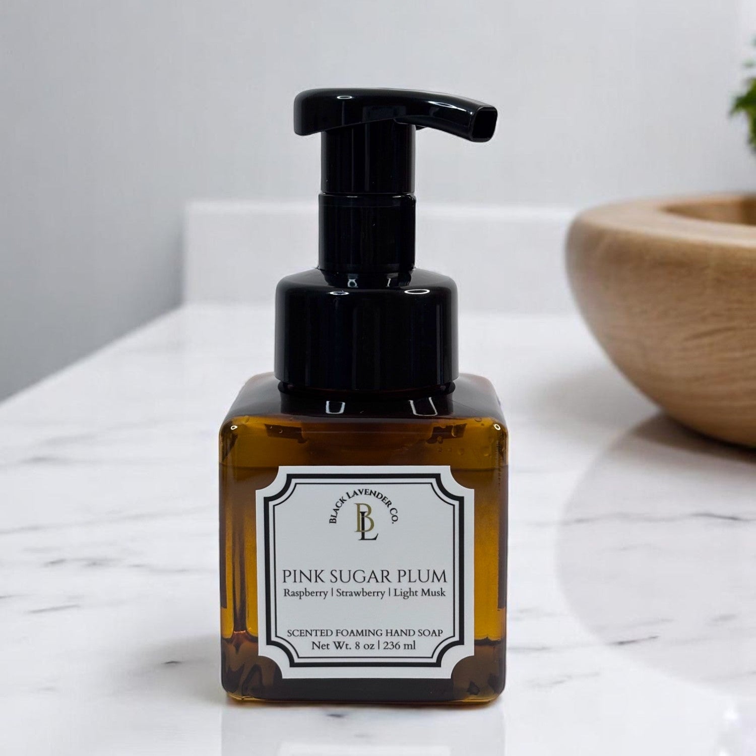 A pump bottle of foaming hand soap labeled 'Pink Sugar Plum' with a black pump dispenser, placed on a marble surface.