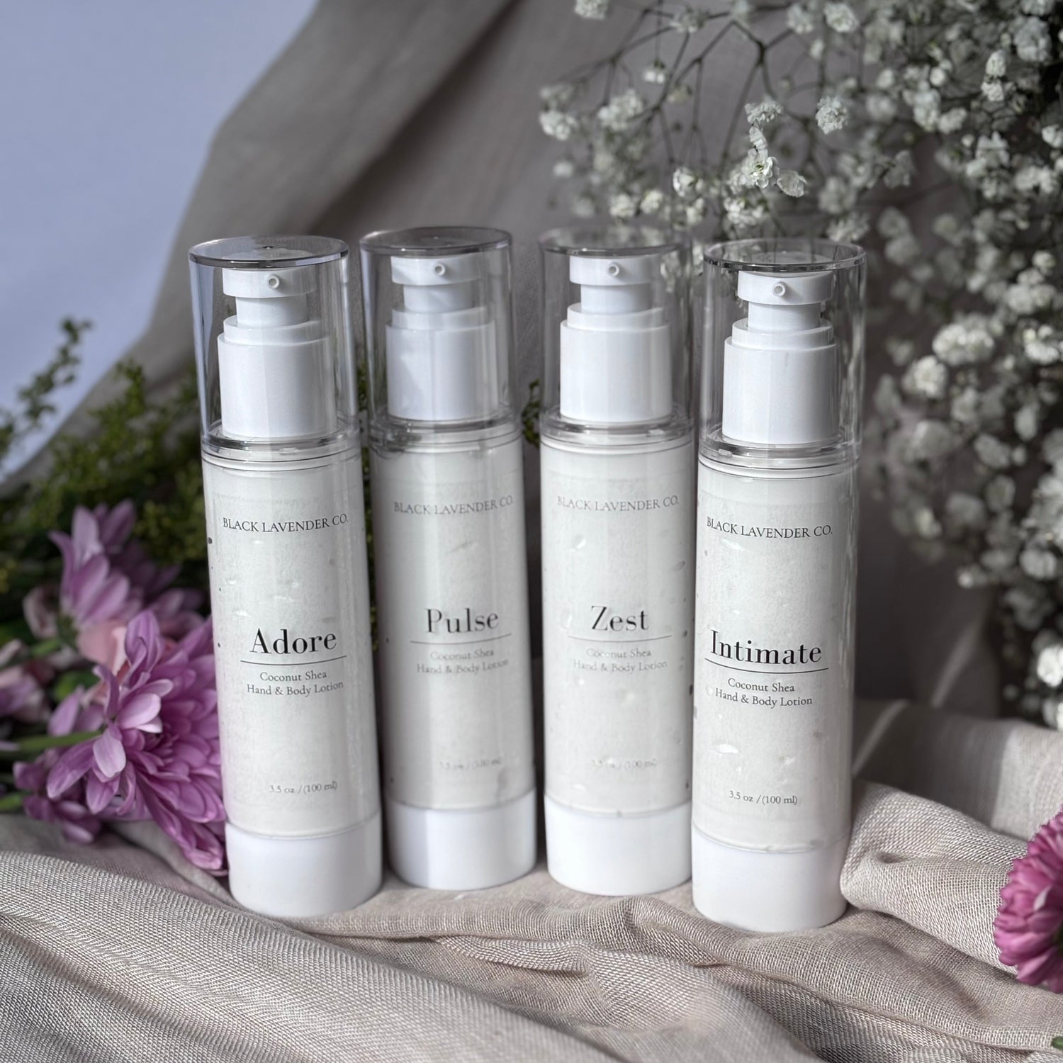 Four skincare bottles labeled 'Adore', 'Pulse', 'Zest', and 'Intimate' on a textured surface with flowers in the background.