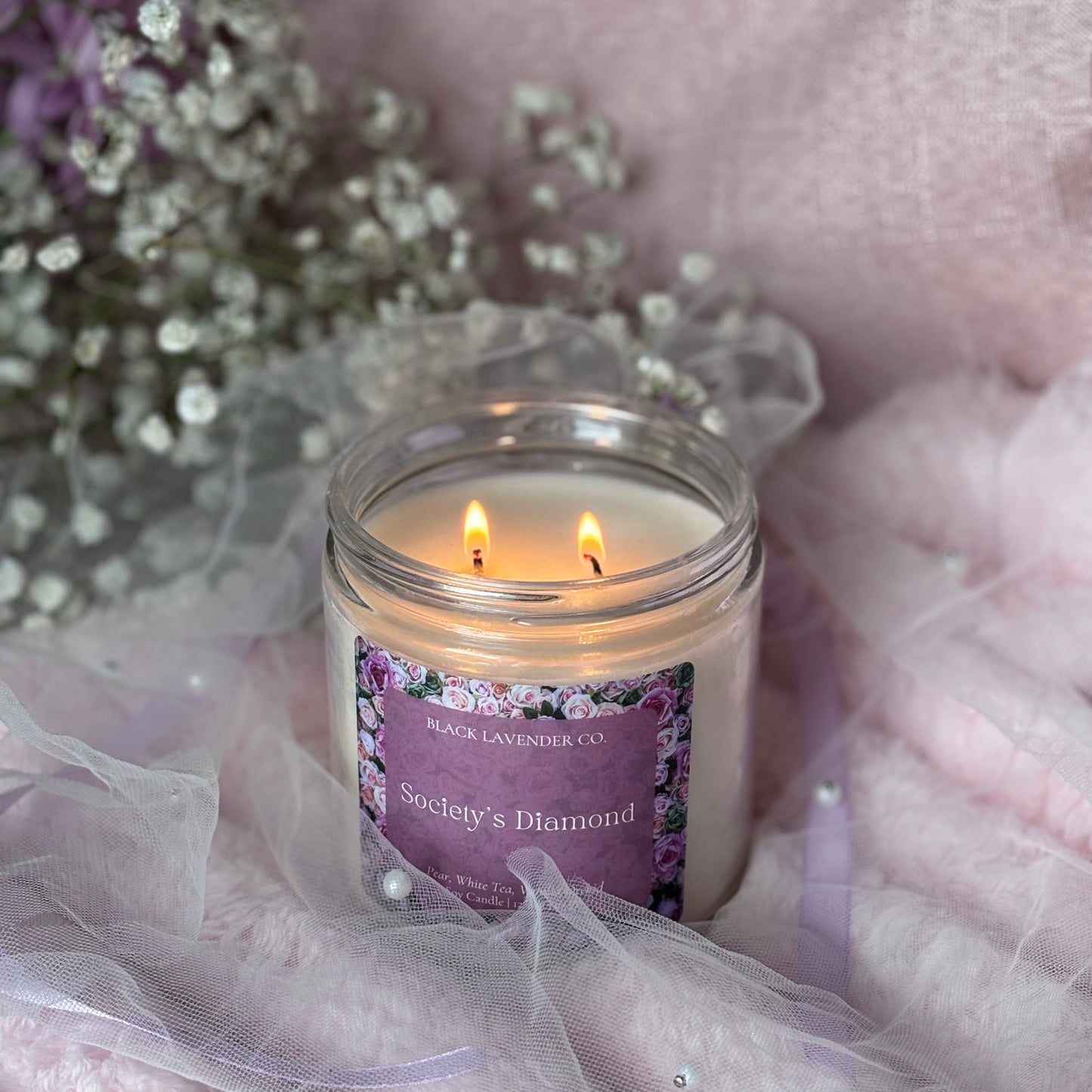 Candle with a purple label on a soft pink fabric background
