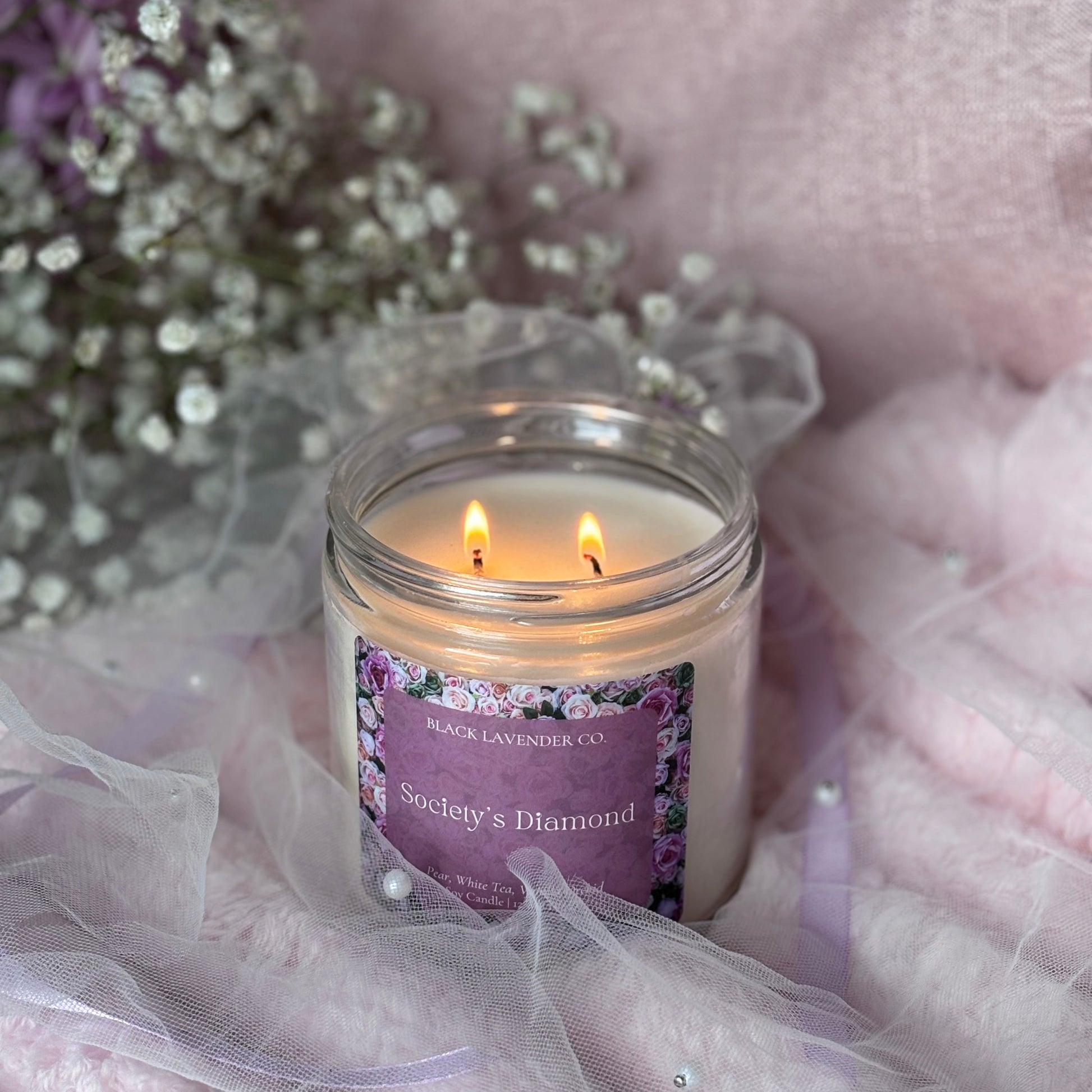 Candle with a purple label on a soft pink fabric background