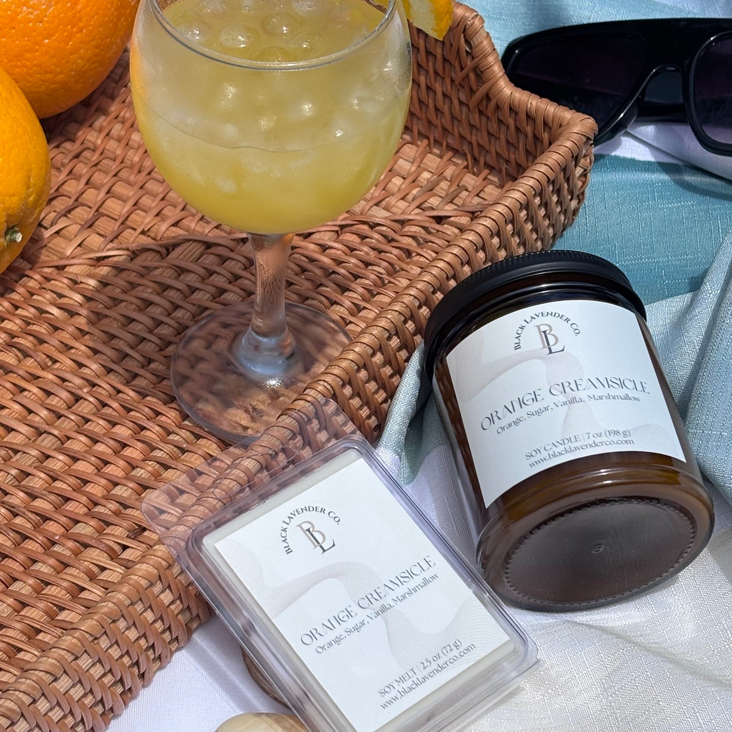 Orange creamsicle candle and wax melts with a glass of orange juice on a woven mat.