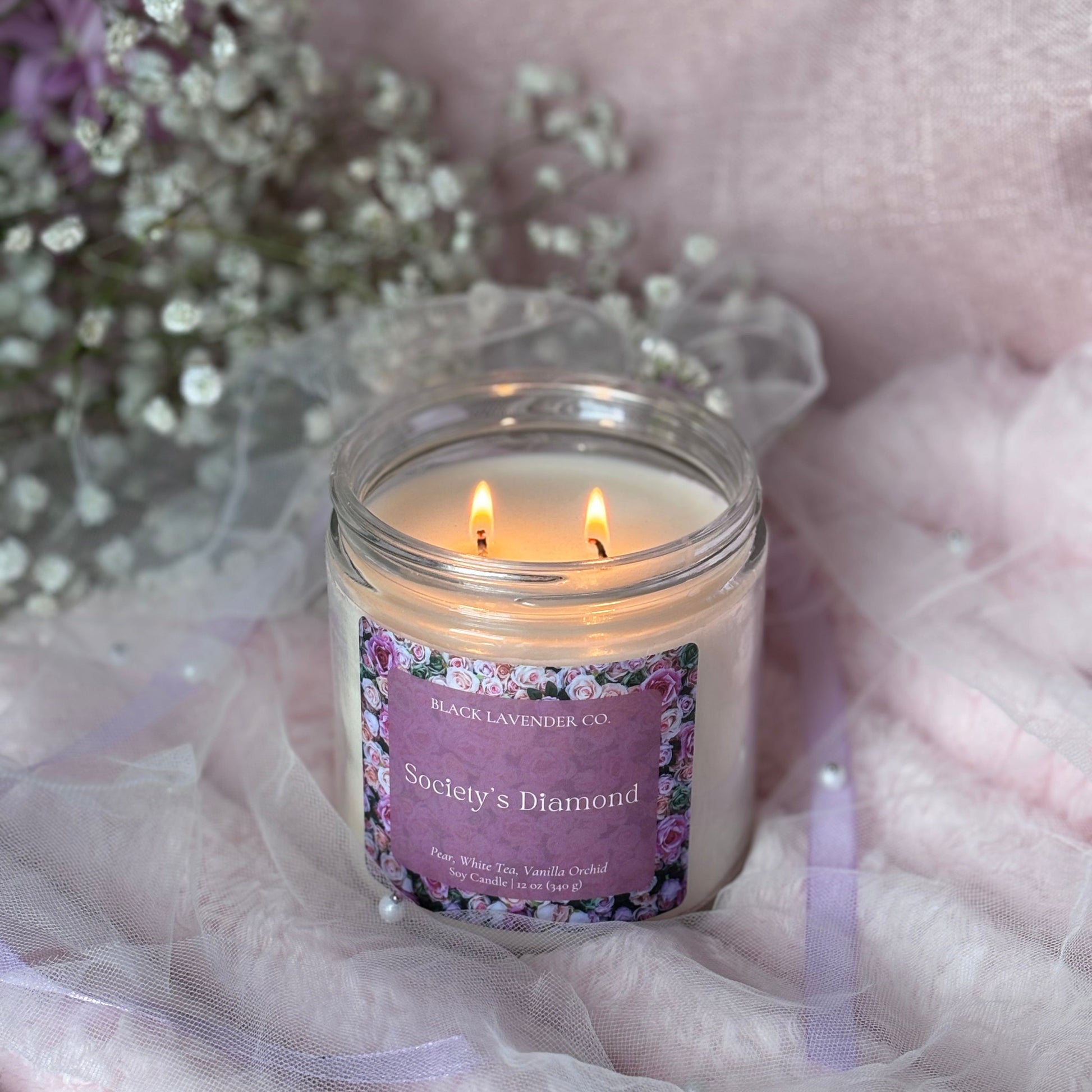 Candle in a glass jar with a purple label on a soft pink fabric background