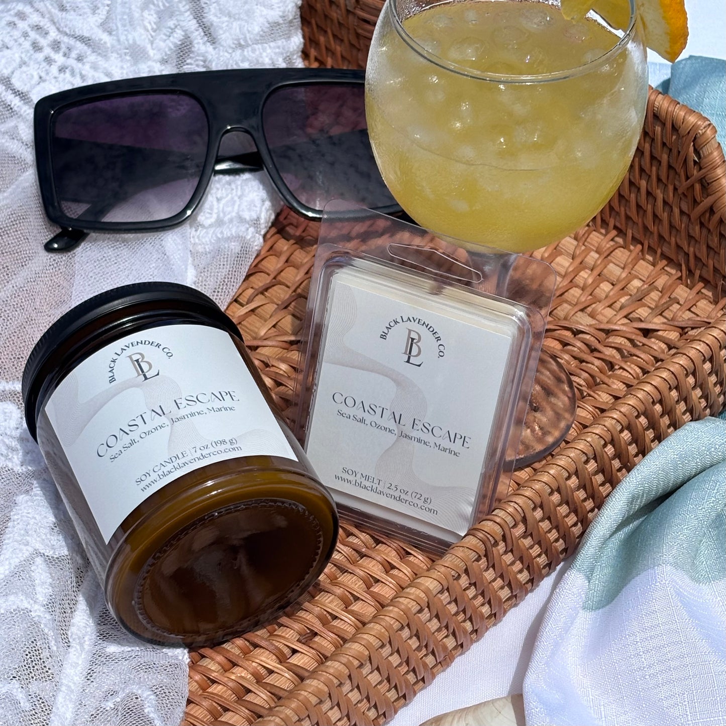 Candle, wax melt, and sunglasses on a woven tray with a glass of lemonade.