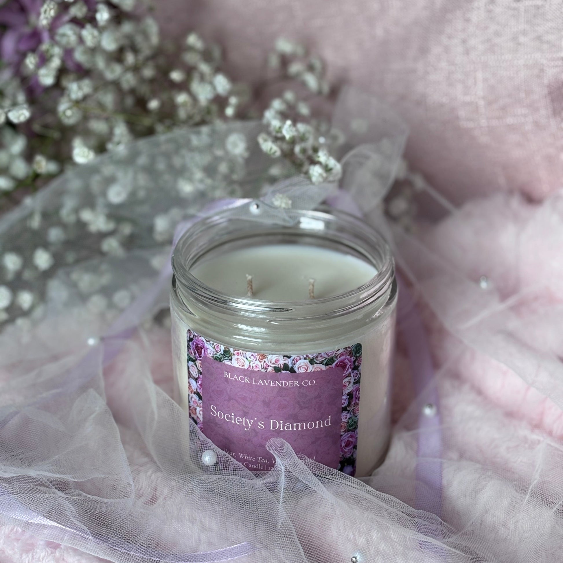 Candle with a purple label on a soft pink fabric background