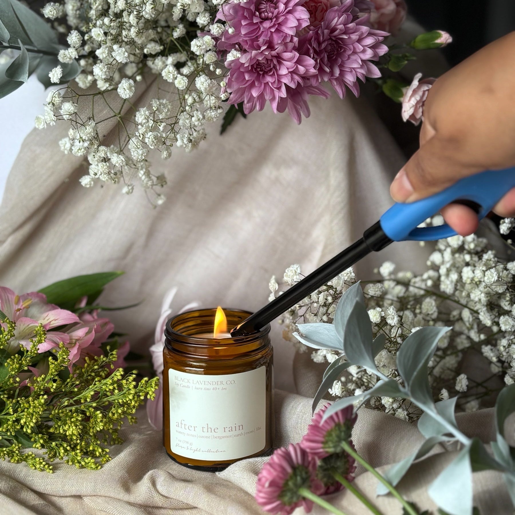 Candle being lit with a match, surrounded by flowers on a soft fabric background