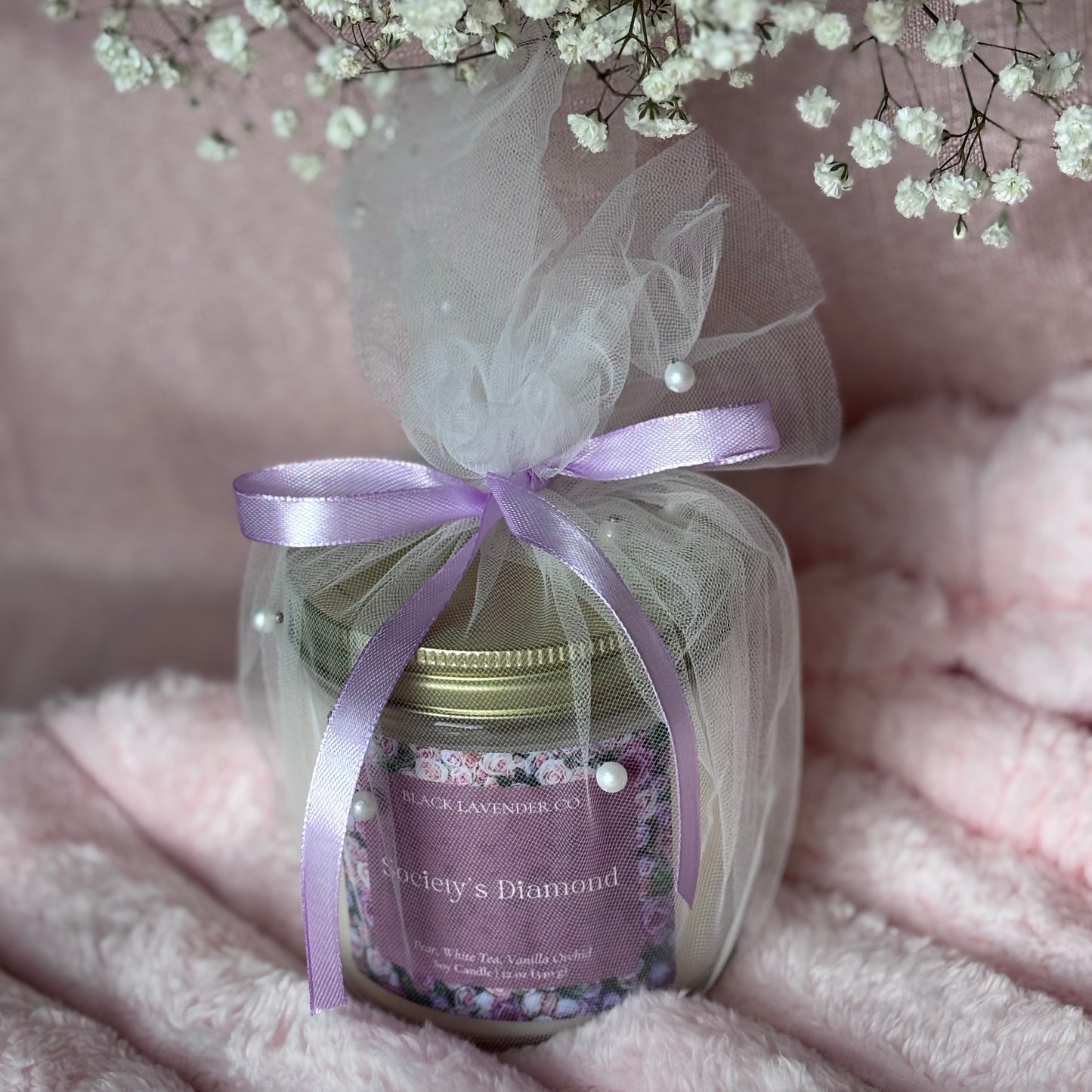 Jar of soy candle with a purple ribbon on a soft pink background