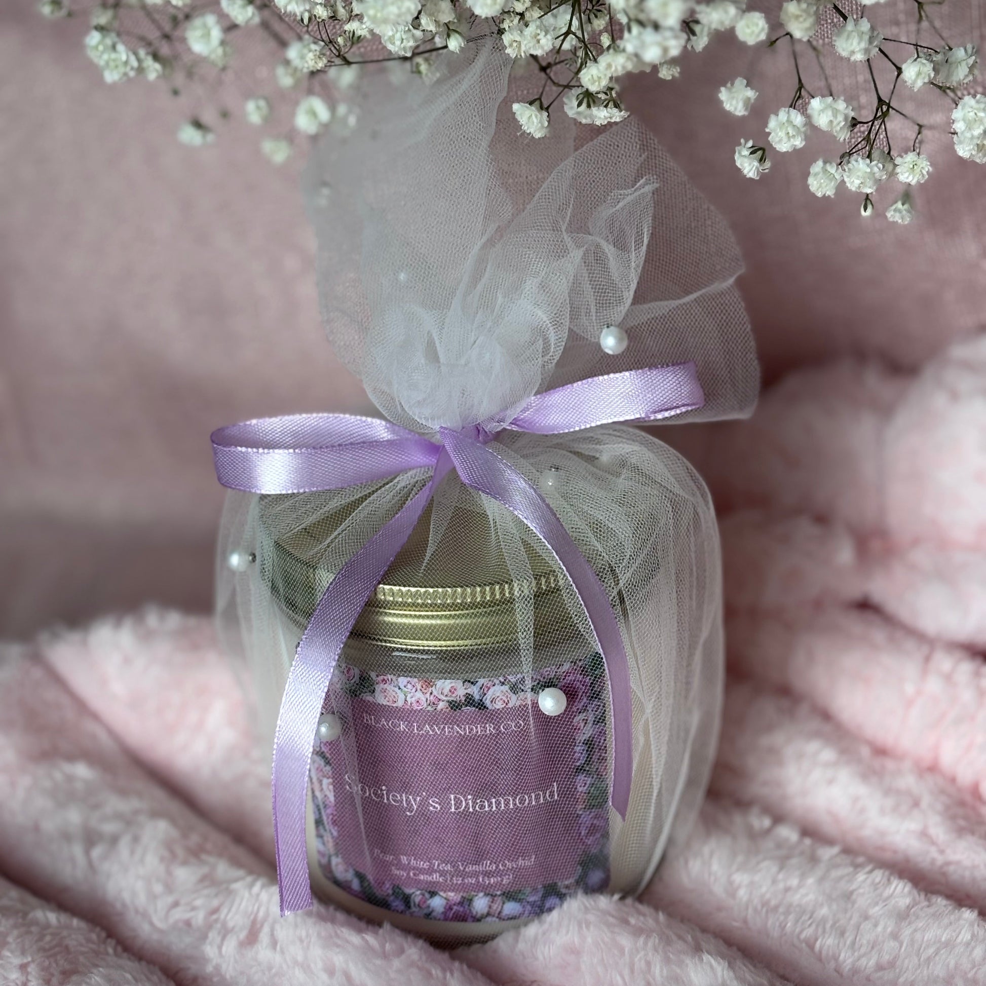 Jar of soy candle with a purple ribbon on a soft pink background